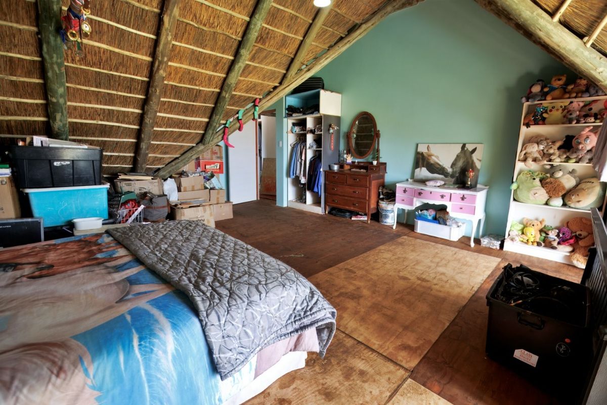 Spacious attic-style bedroom featuring a high vaulted thatched roof, exposed timber beams, and built-in storage cabinetry.