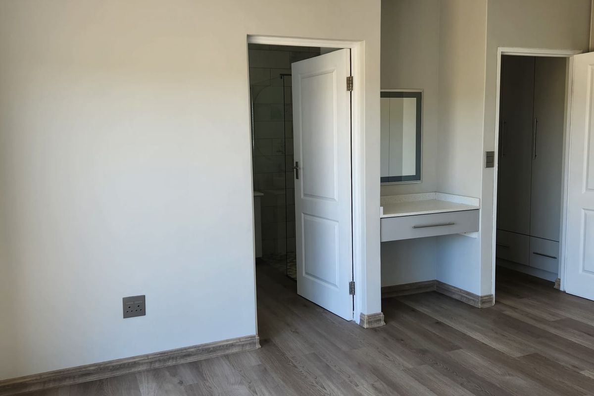 Spacious bedroom featuring modern laminate flooring, built-in vanity, and integrated cupboards, with direct access to an en-suite bathroom.