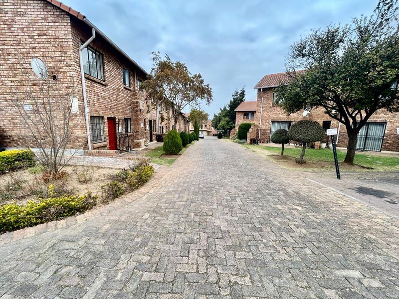 A view of the complex driveway featuring brick townhouse facades, paved surfaces, and established garden areas.