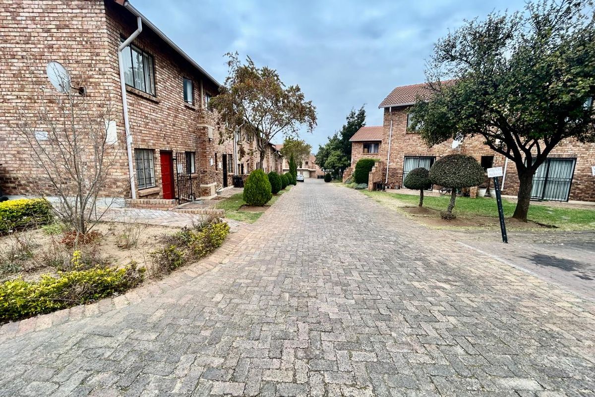 A view of the complex driveway featuring brick townhouse facades, paved surfaces, and established garden areas.