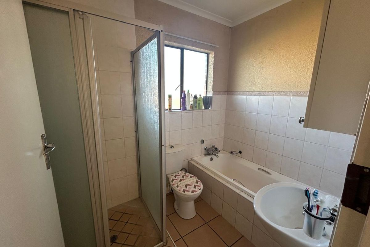 A functional bathroom featuring a separate shower enclosure, bathtub, pedestal sink, and tiled finishes, offering a practical layout with potential for cosmetic updates.