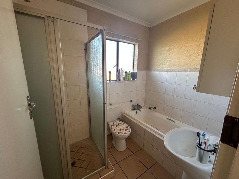 A functional bathroom featuring a separate shower enclosure, bathtub, pedestal sink, and tiled finishes, offering a practical layout with potential for cosmetic updates.