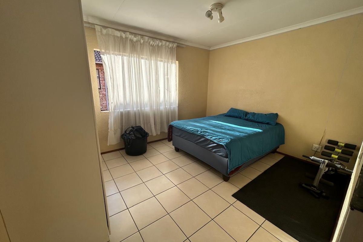 A functional bedroom featuring tiled flooring, a built-in cupboard, and a large window allowing for natural light.