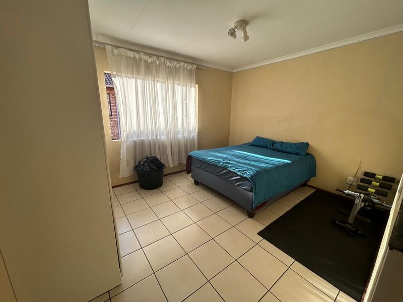A functional bedroom featuring tiled flooring, a built-in cupboard, and a large window allowing for natural light.