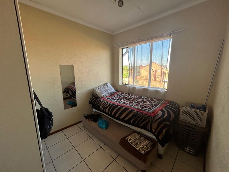 A compact bedroom featuring tiled flooring, a built-in wardrobe, and a window providing natural light and exterior views.