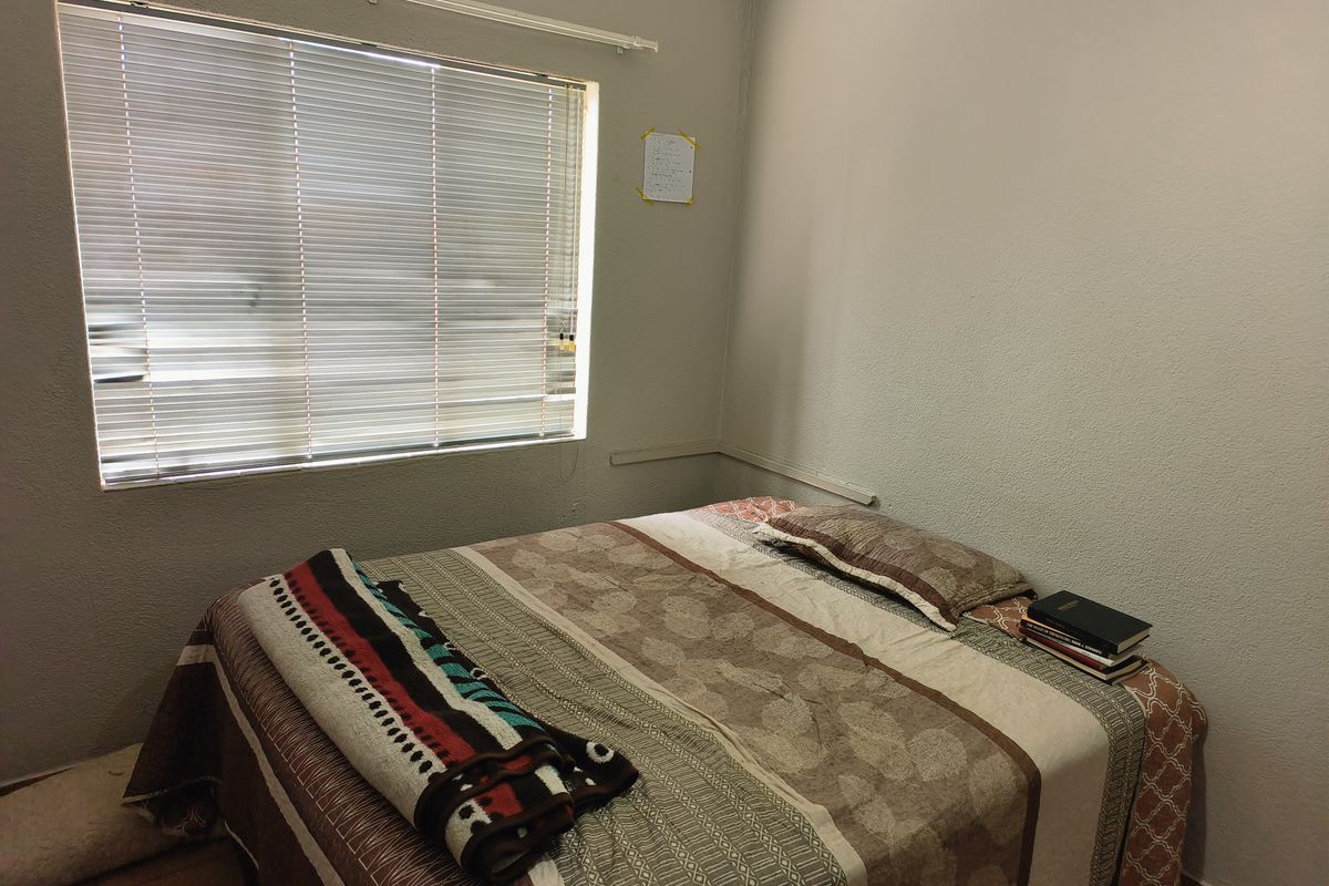 A functional bedroom featuring tiled flooring, a large window with fitted blinds, and neutral wall finishes.
