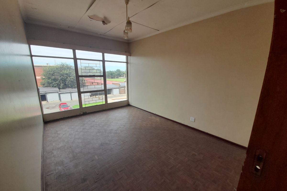 An empty bedroom featuring parquet flooring, large windows with security bars, and a damaged ceiling requiring repair.