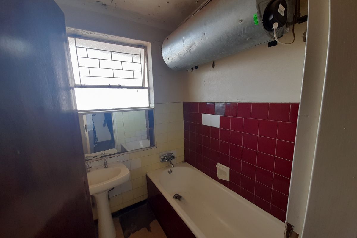 A dated bathroom featuring a pedestal basin, bathtub with red tiled splashback, and an exposed wall-mounted electric water heater.
