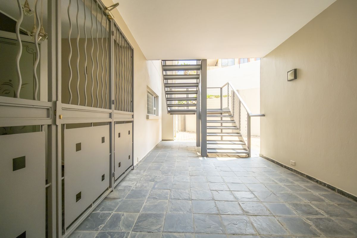 A covered outdoor walkway featuring stone tile flooring, a secure metal gate, and a metal staircase leading to an upper level.