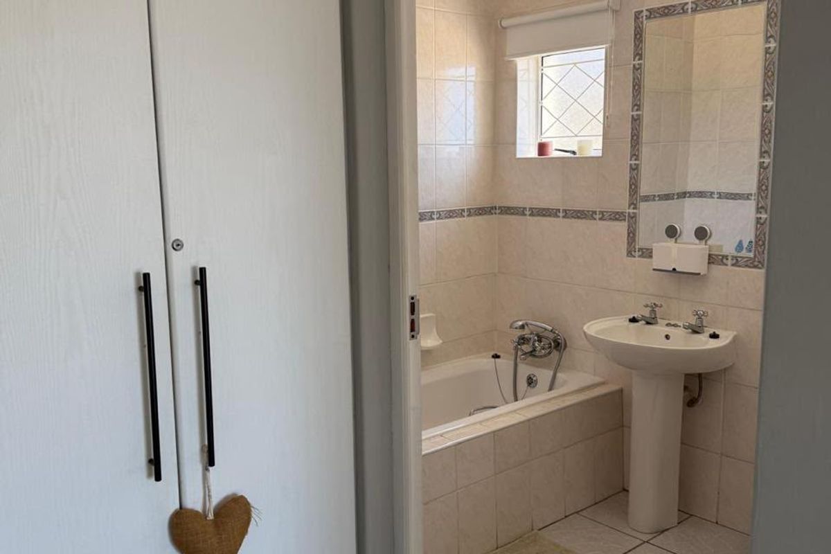 A functional bathroom featuring a pedestal basin, built-in bathtub, and tiled finishes, adjacent to a built-in cupboard in the hallway.