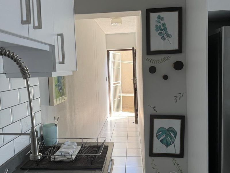A functional kitchen area featuring white cabinetry, subway tile backsplash, and a modern gooseneck faucet, leading into a tiled hallway.