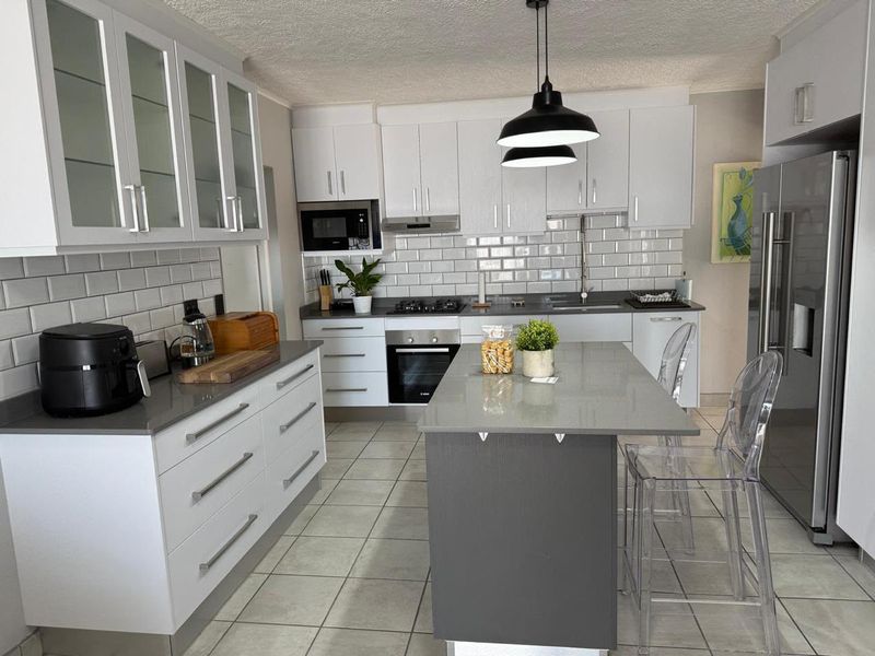 Modern kitchen featuring white cabinetry, grey stone countertops, subway tile backsplash, a central island, and integrated appliances.