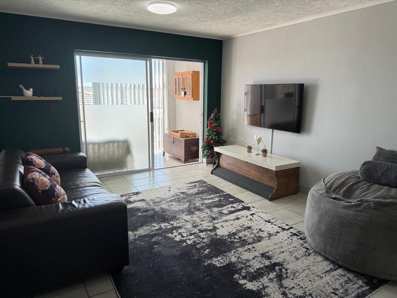 A living room featuring tiled flooring, an accent wall, and a sliding glass door providing access to an outdoor patio area.