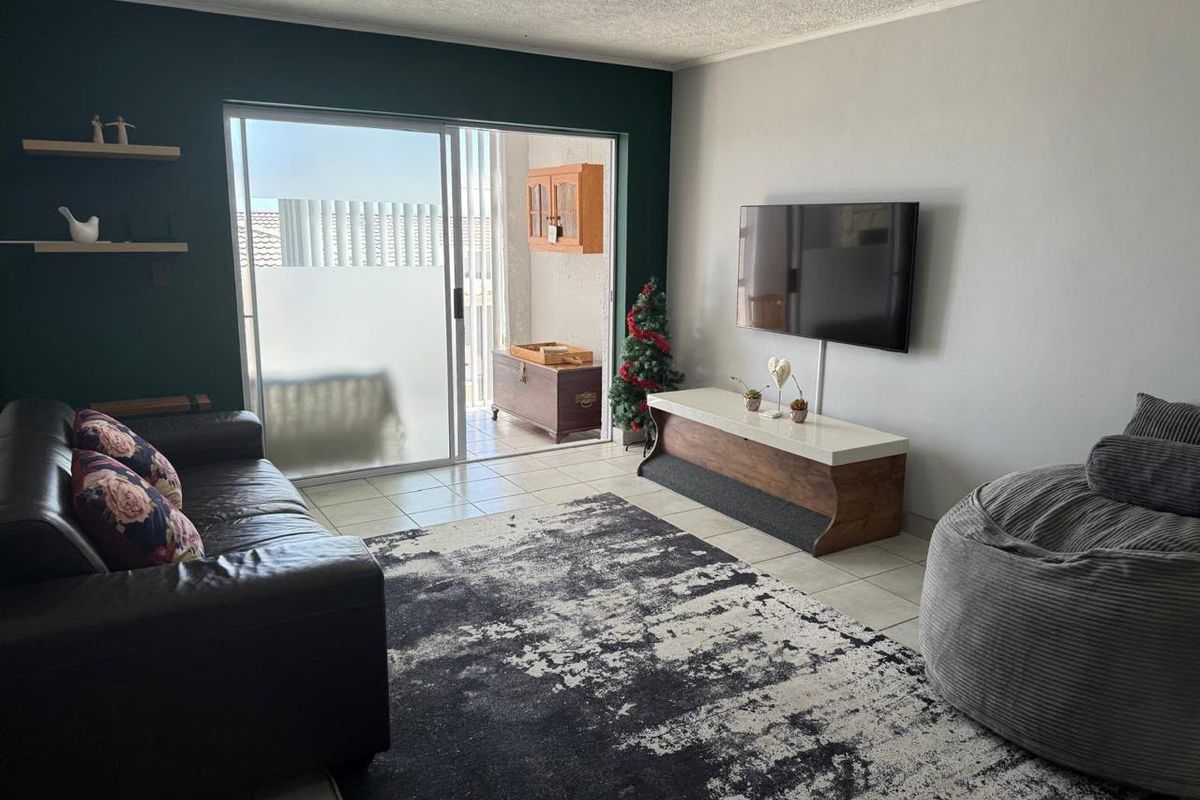 A living room featuring tiled flooring, an accent wall, and a sliding glass door providing access to an outdoor patio area.