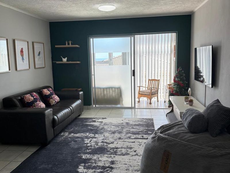 A living room featuring tiled floors, a textured ceiling, floating shelves, and a sliding glass door providing access to an outdoor balcony area.