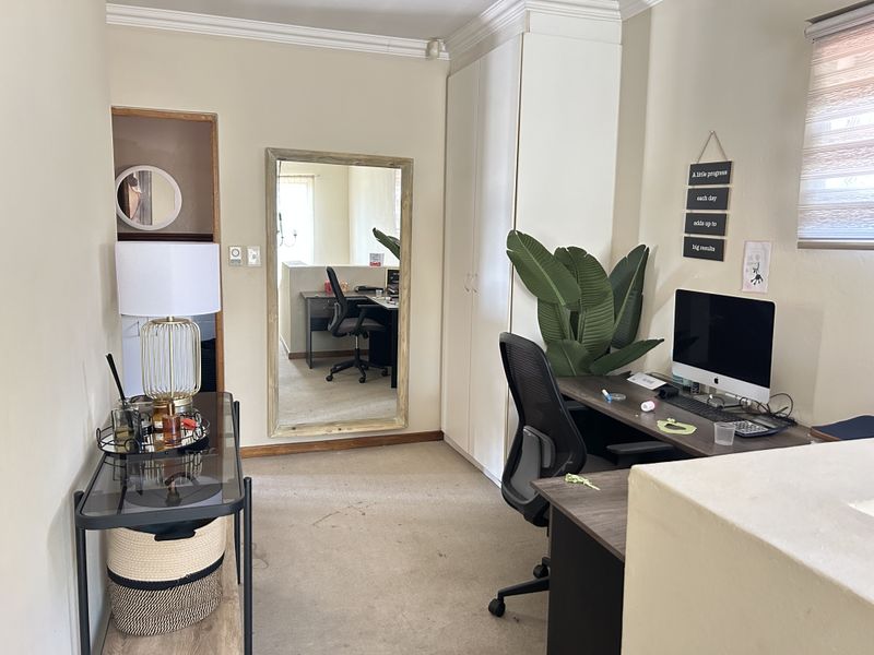 A functional home office space featuring built-in cupboards, neutral wall finishes, and carpeted flooring, suitable for a dedicated workspace.
