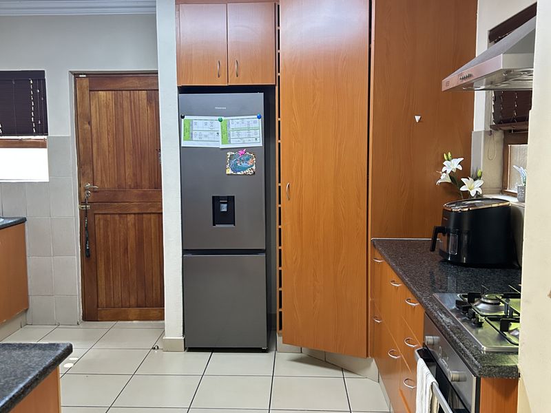 A functional kitchen featuring wood-finish cabinetry, granite countertops, integrated gas hob, electric oven, and tiled flooring with direct access to an adjacent room.