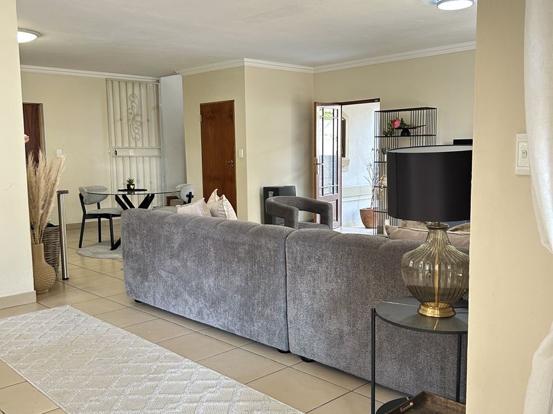 Spacious open-plan living area featuring neutral tiled flooring, coved ceilings, and direct access to an outdoor patio through a wooden door.