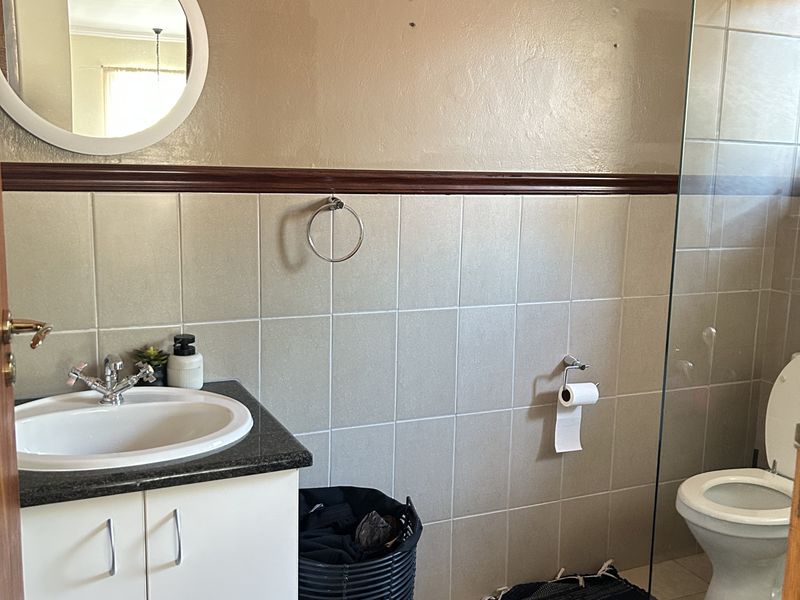 A functional bathroom featuring a vanity with granite countertop, glass shower enclosure with pebble flooring, and neutral wall tiling.