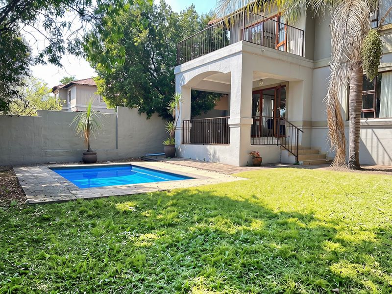 Rear exterior view of the townhouse featuring a private swimming pool, a covered patio, and an upper-level balcony with metal railings.