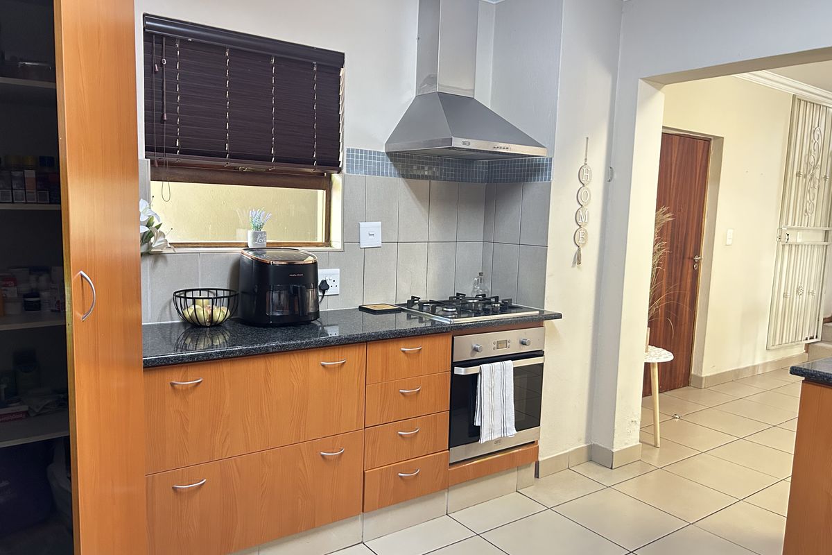 A functional kitchen featuring granite countertops, built-in cabinetry, a gas hob, and a stainless steel extractor fan with tiled flooring throughout.