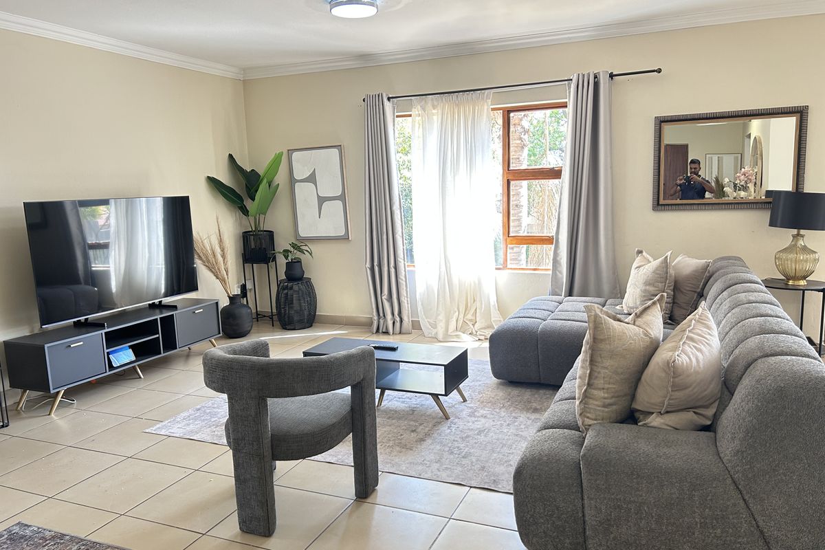 A well-lit living room featuring neutral tiled flooring, crown molding, and a large window that allows for ample natural light.