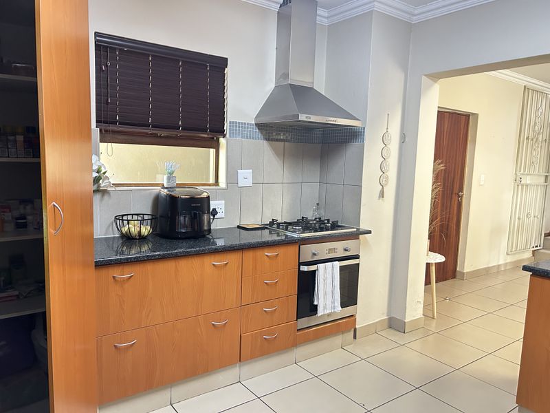 A functional kitchen featuring granite countertops, built-in cabinetry, a gas hob, and a stainless steel extractor fan with tiled flooring throughout.