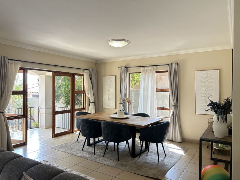 Bright open plan dining area featuring tiled floors, large timber-framed windows, and sliding glass doors providing direct access to the outdoor patio.