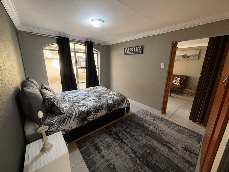 A bedroom featuring tiled flooring, an arched window with natural light, and ceiling cornice detailing, with an adjacent room visible through the doorway.