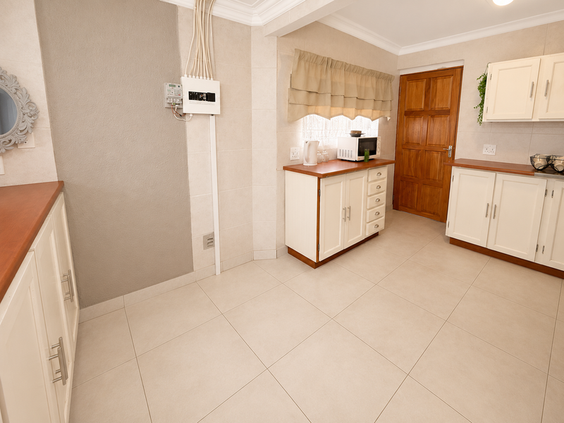 A functional kitchen featuring tiled flooring, built-in cabinetry with laminate countertops, and a solid timber door, with visible electrical infrastructure.