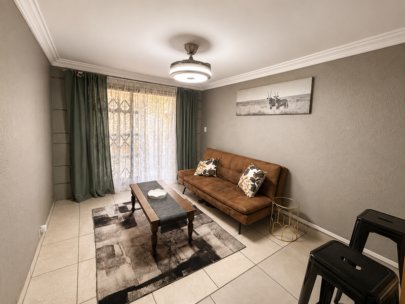 A well-maintained living room featuring tiled flooring, crown molding, a central ceiling fan, and a sliding glass door with an integrated security gate.