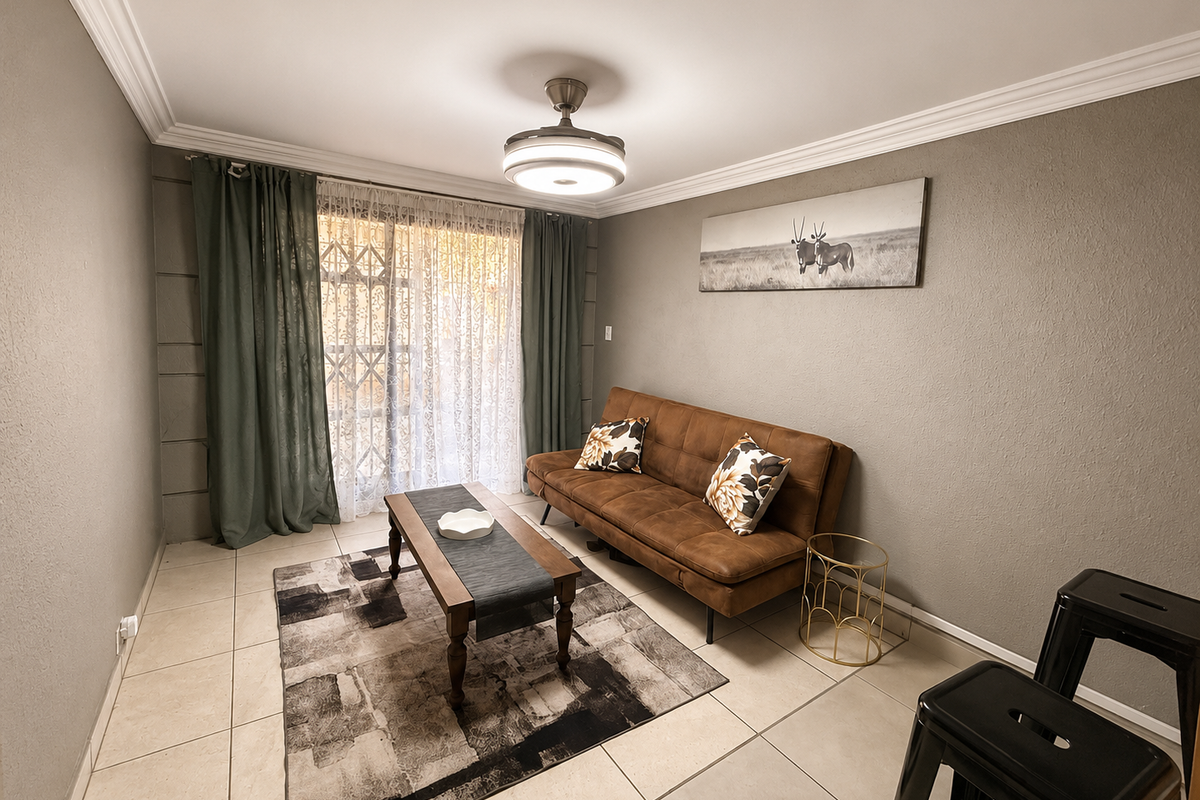 A well-maintained living room featuring tiled flooring, crown molding, a central ceiling fan, and a sliding glass door with an integrated security gate.