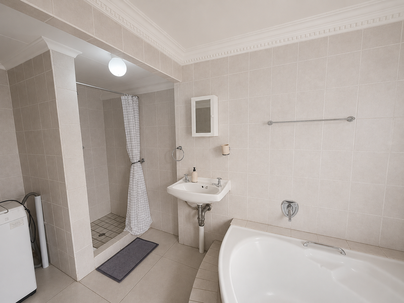 A functional bathroom featuring a corner bathtub, separate shower enclosure, wall-mounted basin, and neutral floor-to-ceiling tiling.