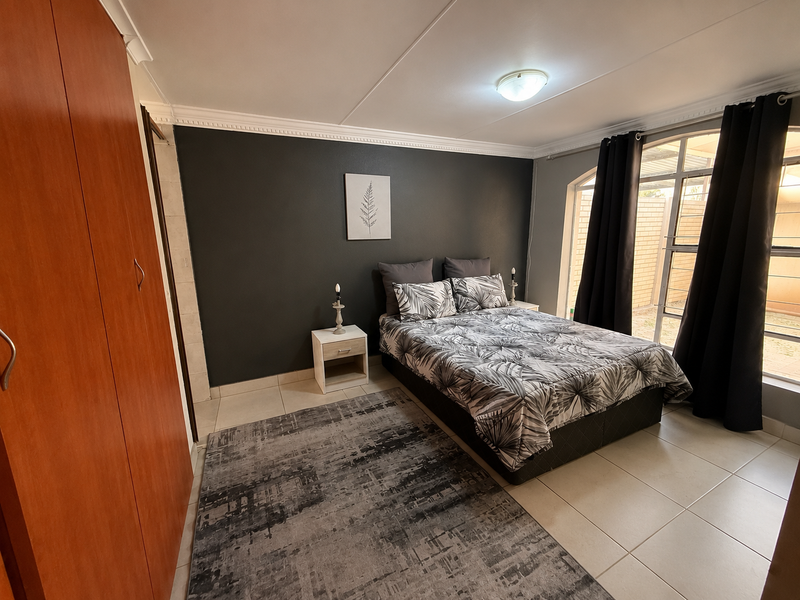 A well-maintained bedroom featuring tiled flooring, a built-in wardrobe, and a large window that provides natural light.