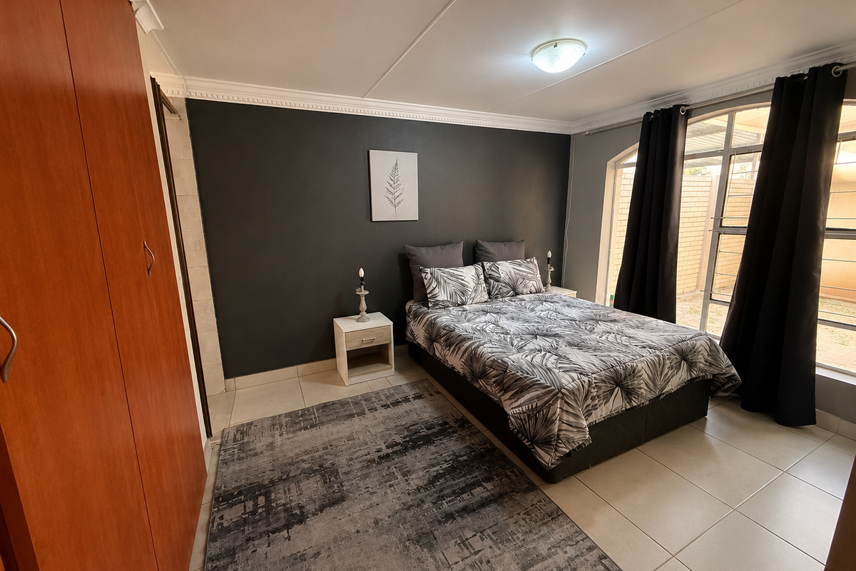 A well-maintained bedroom featuring tiled flooring, a built-in wardrobe, and a large window that provides natural light.