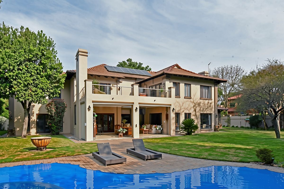 Rear view of a double-story residence featuring a swimming pool, paved deck, covered patio, upper balcony, and solar panels on a tiled roof.