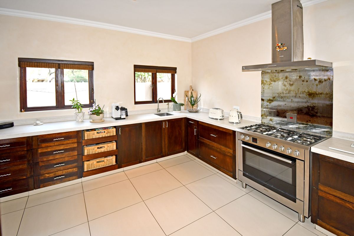 A functional kitchen featuring dark wood cabinetry, stone countertops, a large stainless steel gas range with extractor, and tiled flooring.