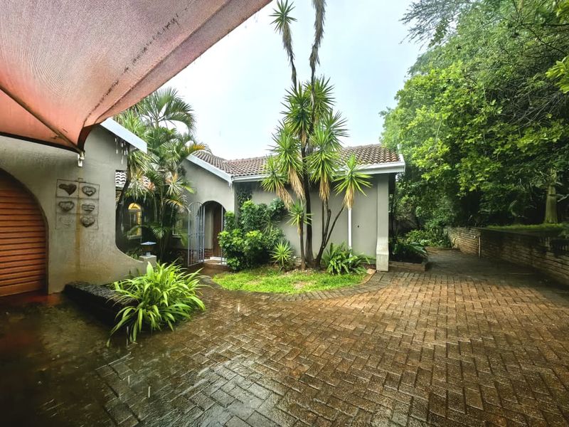 Front exterior view of the property featuring a paved driveway, arched entrance, and a shade sail over the outdoor area.