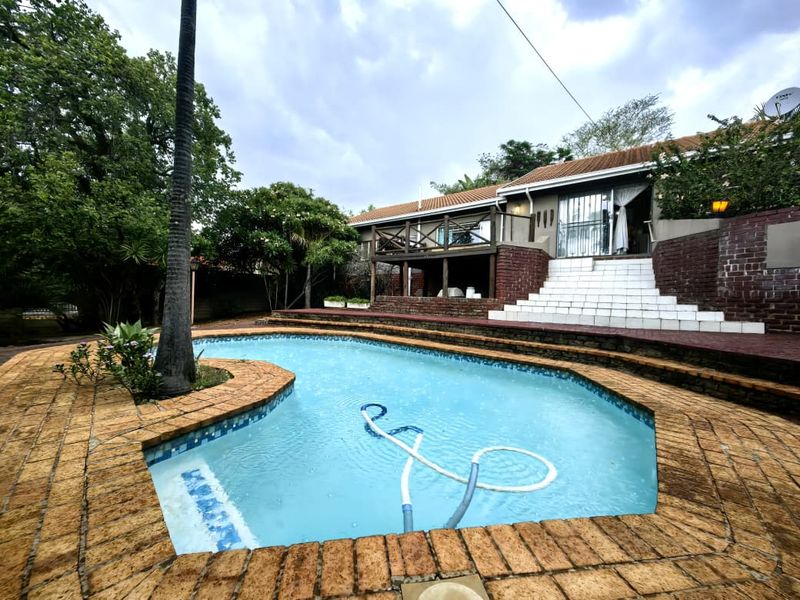 Outdoor pool area featuring a swimming pool, brick paving, a raised wooden deck, and a tiled staircase leading to the rear of the house.