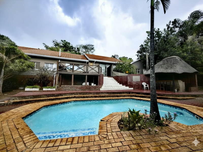 Outdoor entertainment area featuring a swimming pool, raised wooden deck, tiled stairs, and a traditional thatched lapa set in a landscaped garden.