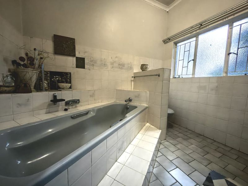 A dated bathroom featuring a built-in bathtub, tiled walls and flooring, and a metal-framed window. The space offers potential for a modern renovation.