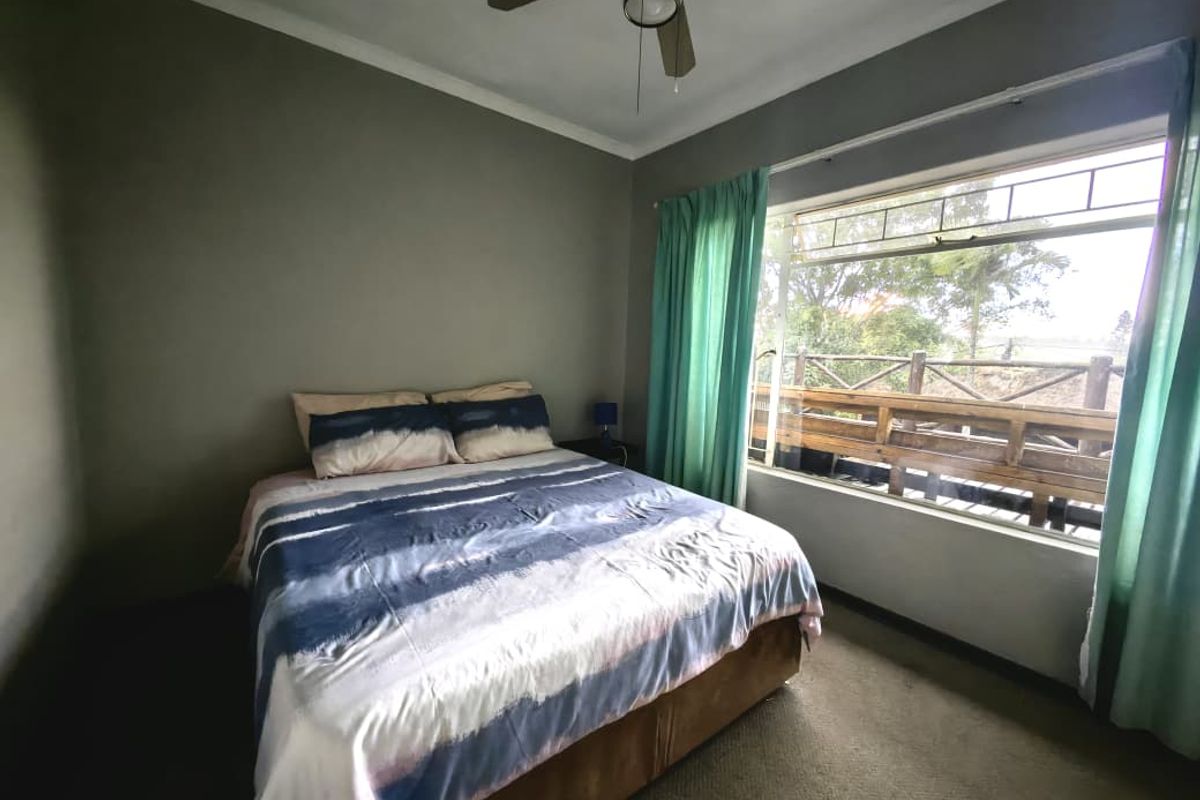 A bedroom featuring a ceiling fan, carpeted flooring, and a large window with views of an outdoor wooden deck.