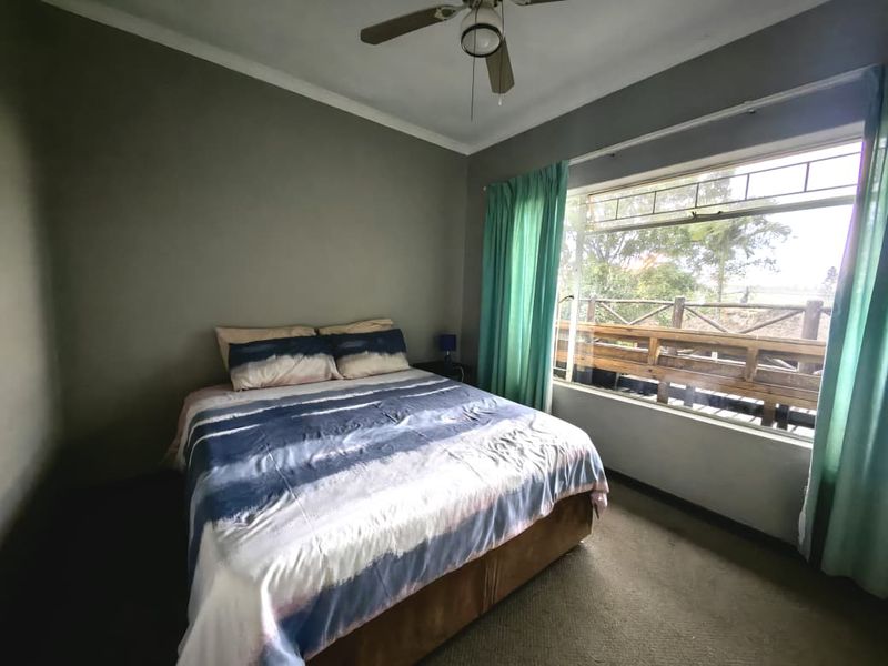 A bedroom featuring a ceiling fan, carpeted flooring, and a large window with views of an outdoor wooden deck.