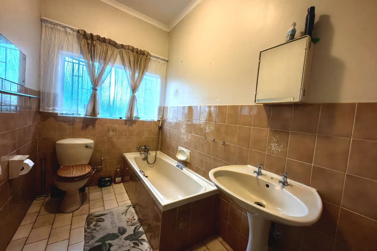 A dated bathroom featuring a bathtub, pedestal basin, and toilet with original ceramic wall and floor tiling.