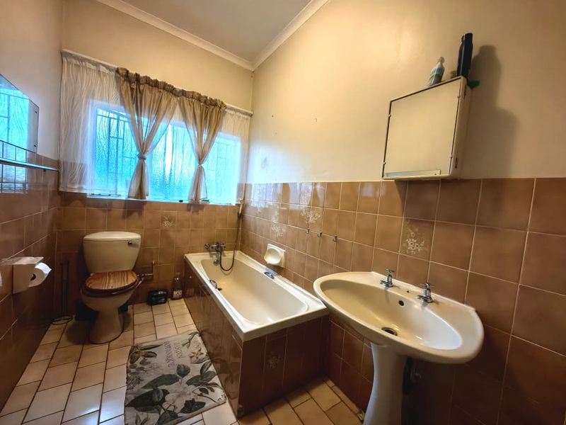 A dated bathroom featuring a bathtub, pedestal basin, and toilet with original ceramic wall and floor tiling.