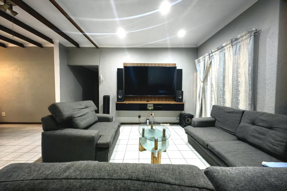 A spacious living room featuring tiled flooring, exposed ceiling beams, and a built-in media console wall unit.