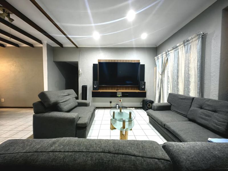 A spacious living room featuring tiled flooring, exposed ceiling beams, and a built-in media console wall unit.