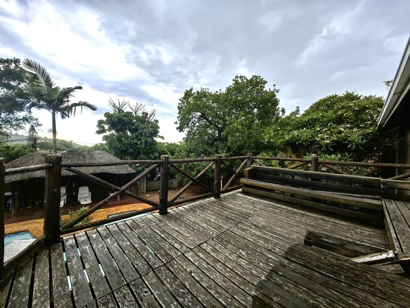 An elevated timber deck featuring a built-in bench and balustrade, overlooking the garden and pool area, requiring maintenance to restore the wood finish.