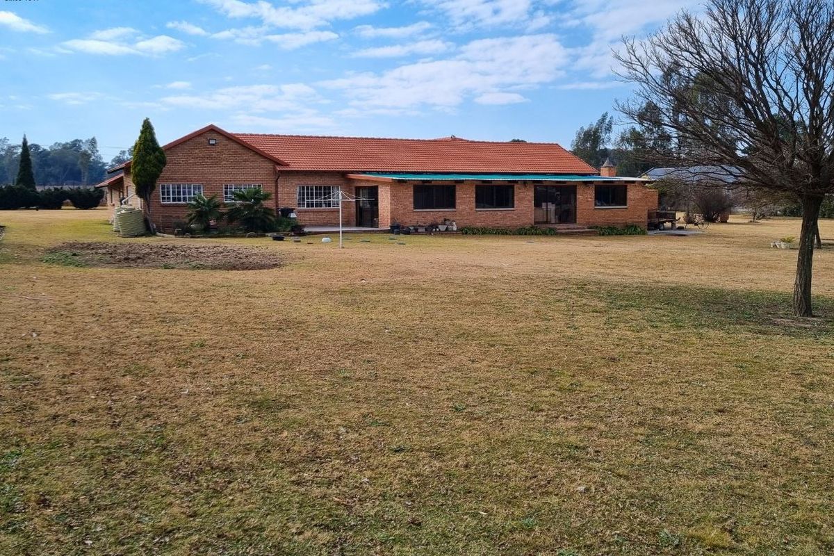 Rear view of a face-brick small holding residence featuring a tiled roof and a covered patio area set within a large garden.