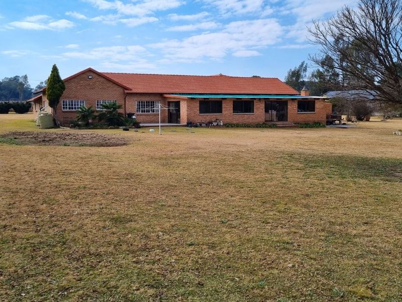 Rear view of a face-brick small holding residence featuring a tiled roof and a covered patio area set within a large garden.